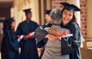 Woman in graduation cap and gown hugging an older woman with gray hair